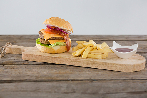 Burger with French fries and sauce on cutting board against wall