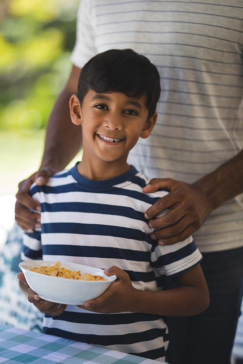 Portrait of smiling boy standing with his father while holding breakfast