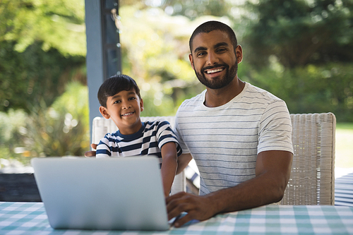 Portrait of smiling young man with his son using laptop at table
