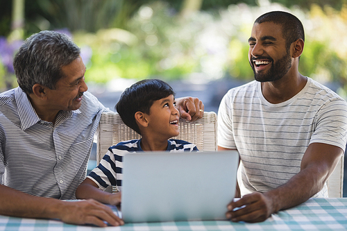 Happy multi-generation family sitting by laptop on table at porch