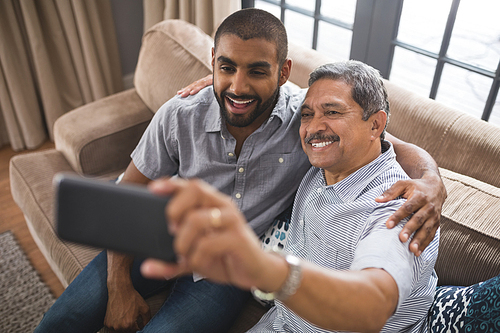 Happy man with his son taking selfie while sitting together on couch at home