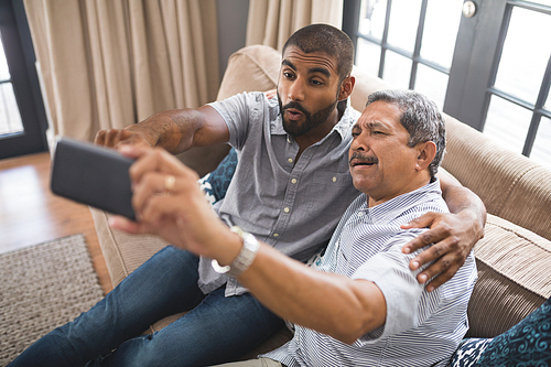 Happy man with his father taking selfie while sitting together on couch at home