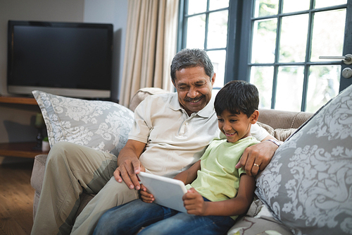 Smiling boy with grandfather using digital tablet while sitting on couch at home