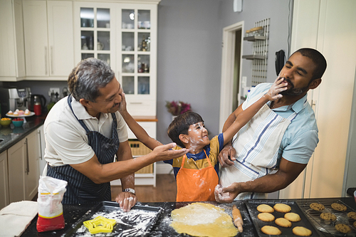 Boy playing with father and grandfather while preparing food together in kitchen at home