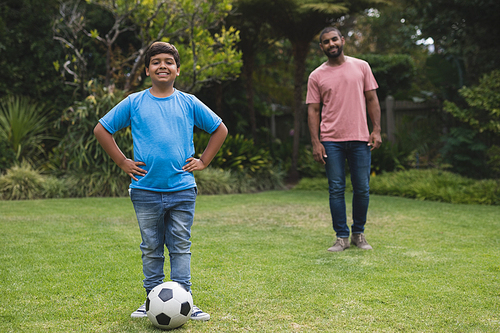 Portrait of smiling boy standing by soccer ball with father in background at park