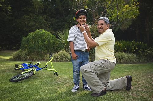 Portrait of grandfather helping grandson for wearing bicycle helmet at park