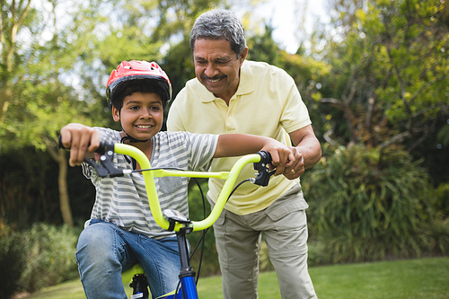 Grandfather assisting grandson while riding bicycle at park