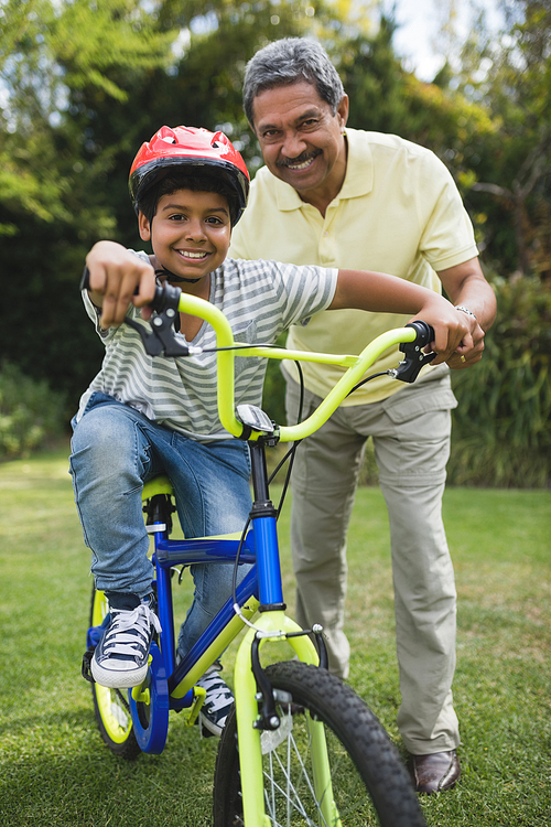 Portrait of grandfather assisting grandson while riding bicycle at park