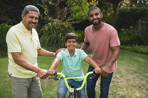 Happy father and grandfather helping boy while riding bicycle at park