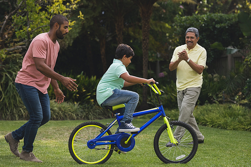 Father and grandfather motivating boy while riding bicycle at park