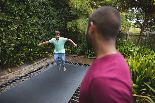 Side view of father looking at son jumping on trampoline