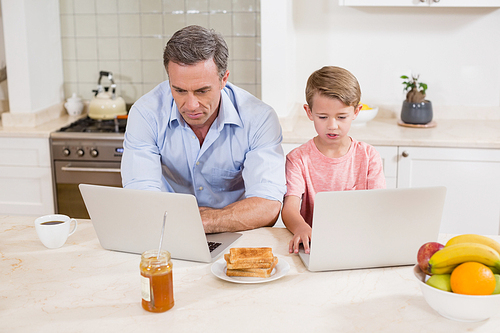 Father and son using laptop in kitchen at home