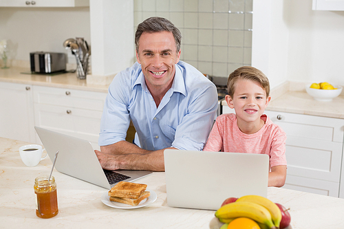 Portrait of smiling father and son with laptop in kitchen