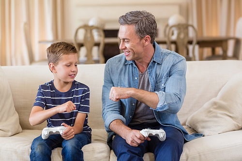 Father and son giving fist bump to each other while playing video game in living room at home