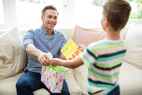 Father receiving a gift from his son in living room at home