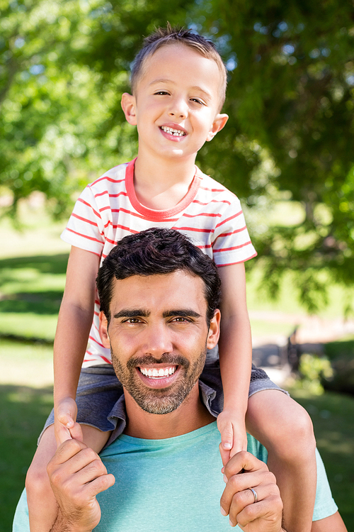 Portrait of smiling father carrying his son on shoulders in the park