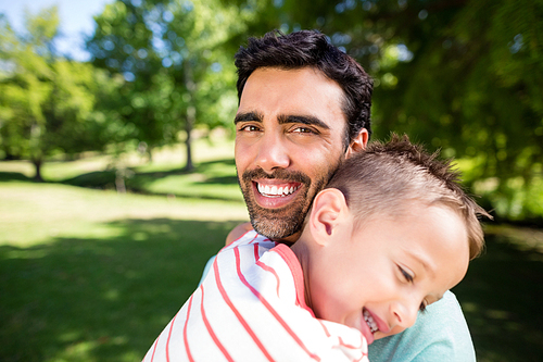 Father smiling while embracing his son in park on a sunny day