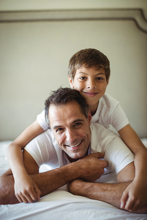 Portrait of father and son smiling while lying on bed