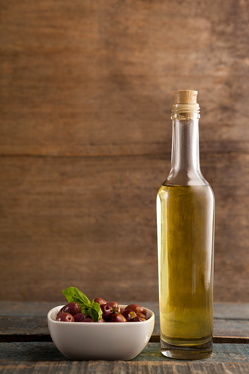 Black olive in container by bottle on table against wall