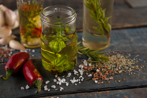 Jalapeno pepper by spices and herbs with oil in containers on wooden table