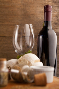 Wine bottle by glass with spice and bread on table against wooden wall