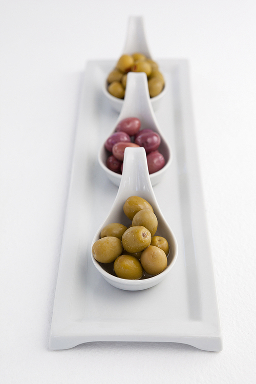 High angle view of green and black olives in containers on tray against white background