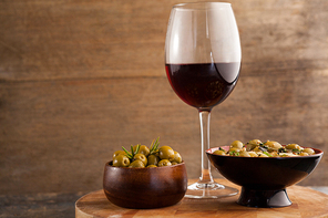 Olives served in bowls by wineglass on table against wooden wall