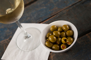 Cropped image of wineglass by green olives served in container on wooden table
