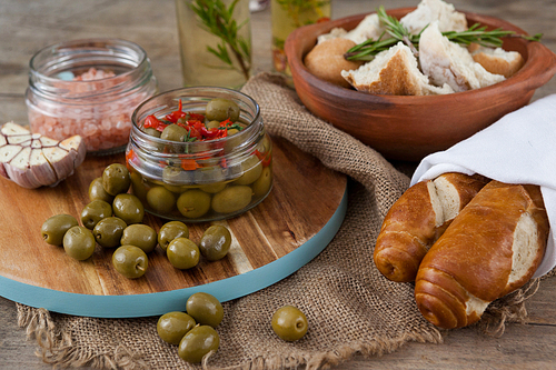 Green olives with containers on cutting board by bread at table