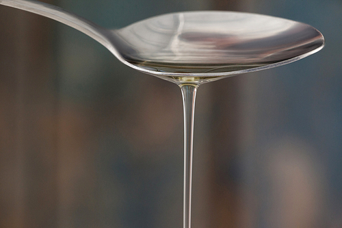 Close up spoon pouring olive oil