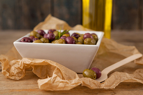 Close up of olives served in bowl by wooden spoon on wax paper