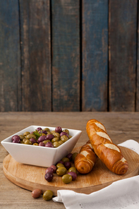 Olives in container by bread on cutting board at table against wall