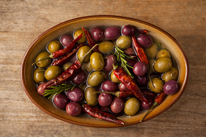 Olives and red chili pepper with oil in wooden container on table