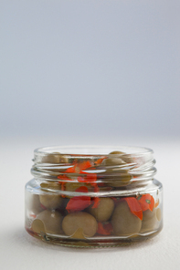 Close up of green olives and herbs in glass jar on table against wall