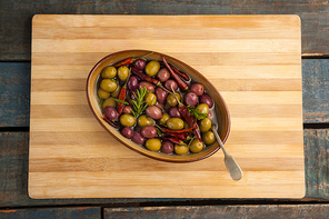 Olives with red chili pepper in container on cutting board at wooden table