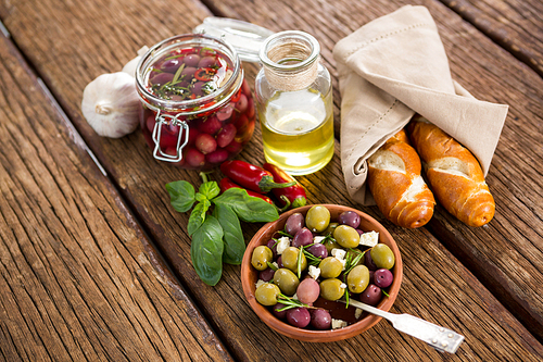 Pickled olives with ingredients and bread on wooden table