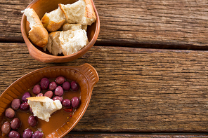 Marinated olives and bread pieces in bowl on wooden table
