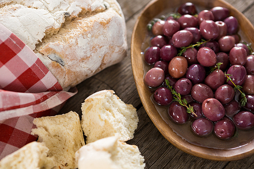 Close-up of marinated olives with bread loaf on wooden table