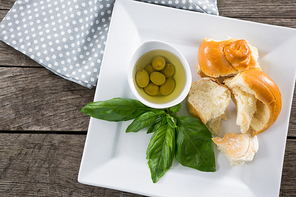Pickled olives with herbs and bread in platter on wooden table