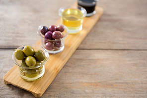 Close-up of marinated olives with olive oil and balsamic vinegar in glass container on a wooden tray