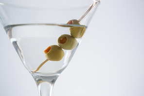 Close-up of cocktail martini with olives on table against white background