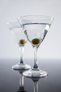 Close-up of cocktail martini with olives on table against white background