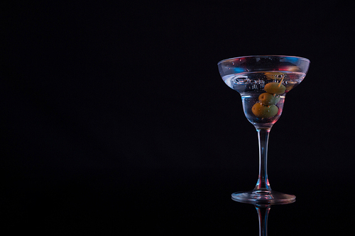Close-up of cocktail martini with olives on table against black background