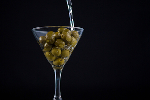 Martini pouring into glass with olives against black background