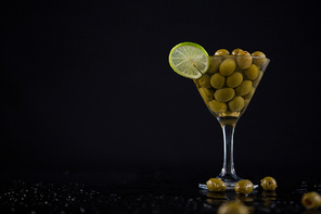 Close-up of cocktail martini with olives and lime on table against black background