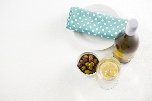 Overhead marinated olives with glass and bottle of wine on white background