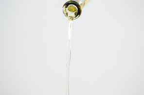 Green olive oil being poured from bottle against white background