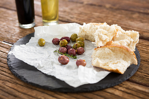 Marinated olives and bread slices kept on tray on wooden table