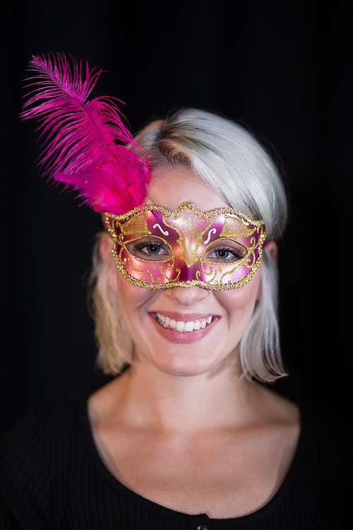 Woman wearing masquerade mask against black background