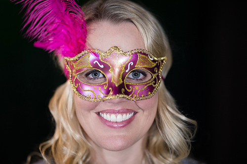 Woman wearing masquerade mask against black background